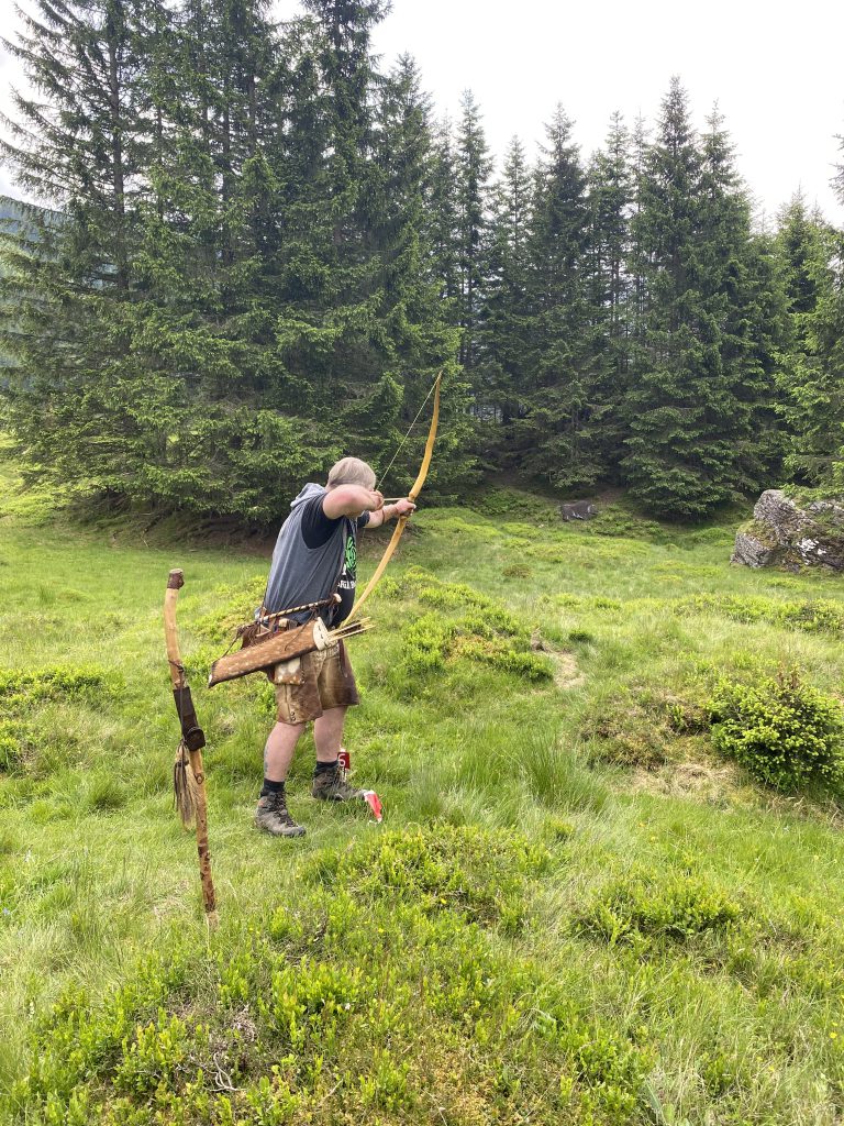 Bogenschütze zielt mit traditionellem Jagdbogen im grünen Raurisertal auf 3D-Parcoursziel
