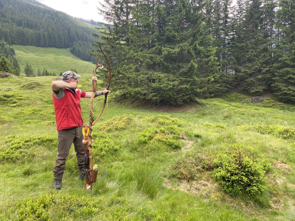 Bogenschütze spannt Jagdbogen auf grünem 3D-Parcours im Raurisertal vor Bergkulisse