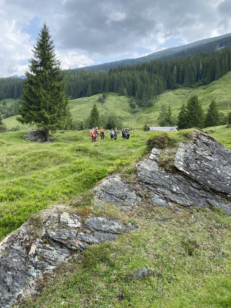 Bogenschütze spannt Jagdbogen auf grünem 3D-Parcours im Raurisertal vor Bergkulisse