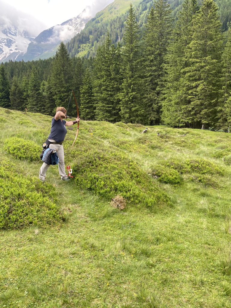 Bogenschütze spannt Jagdbogen auf grünem 3D-Parcours im Raurisertal vor Bergkulisse