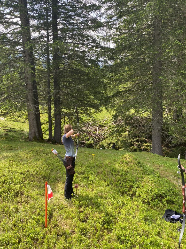 Bogenschütze spannt Jagdbogen auf grünem 3D-Parcours im Raurisertal vor Bergkulisse