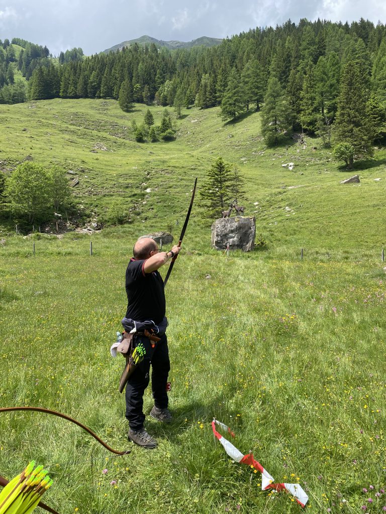 Bogenschütze spannt Jagdbogen auf grünem 3D-Parcours im Raurisertal vor Bergkulisse