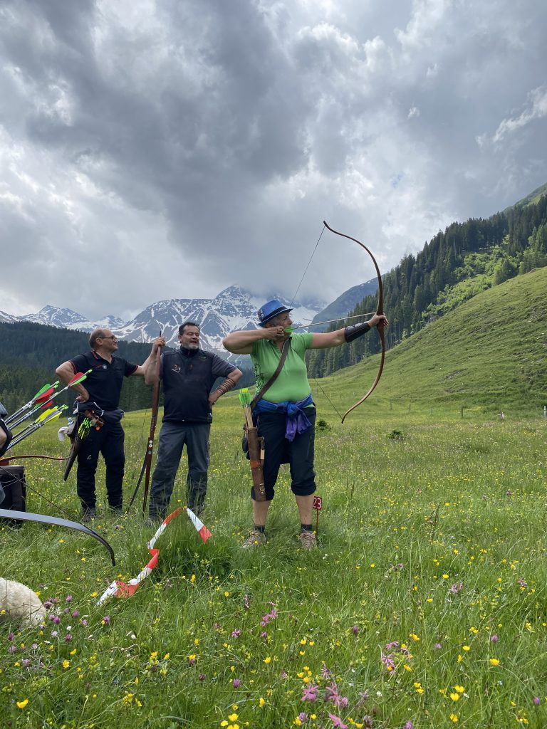 Bogenschütze spannt Jagdbogen auf grünem Parcours im Raurisertal, Natur und Berge im Hintergrund