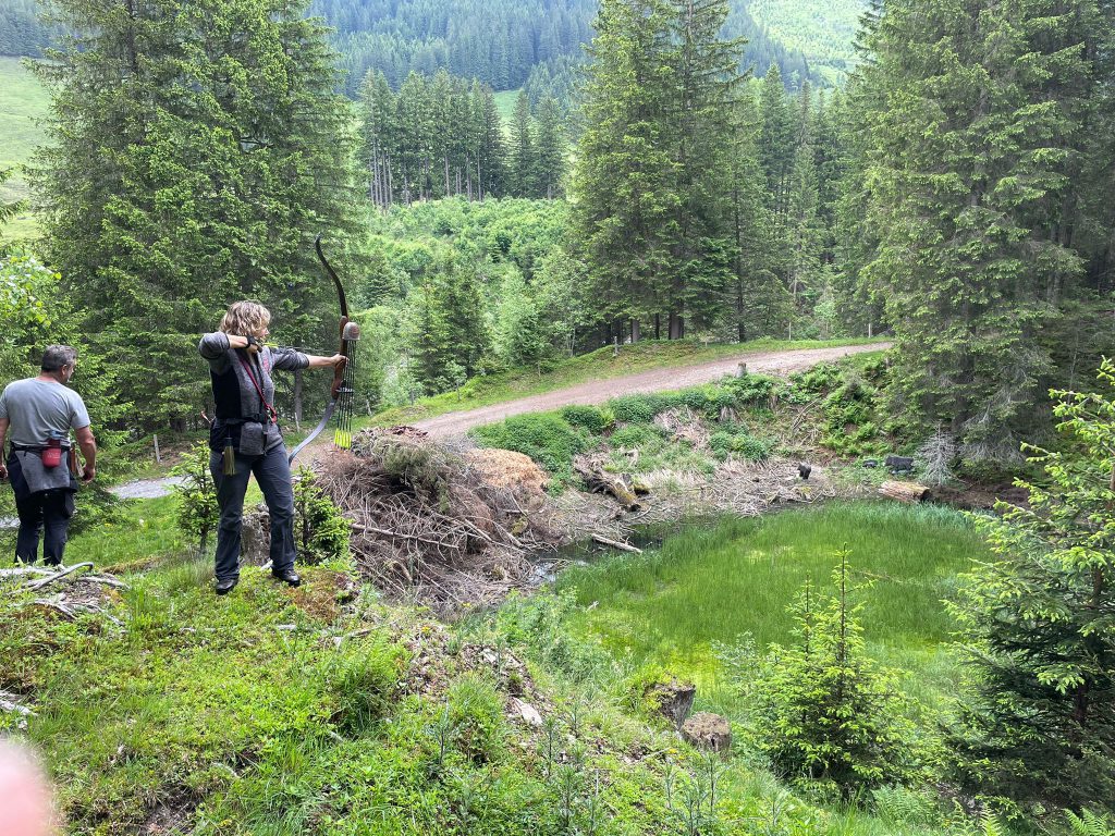 Bogenschütze zielt mit Jagdbogen im grünen Raurisertal, umgeben von Natur und Parcourszielen