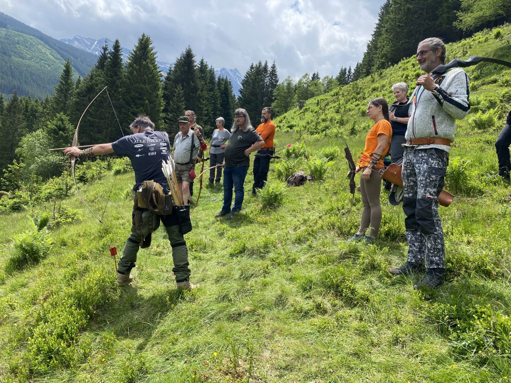 Bogenschütze spannt Jagdbogen auf grünem 3D-Parcours im Raurisertal vor Bergkulisse