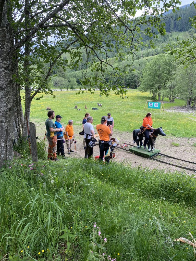 Bogenschütze spannt Jagdbogen auf grünem 3D-Parcours im Raurisertal, Natur im Hintergrund
