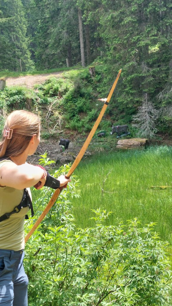 Bogenschütze spannt Jagdbogen auf grünem 3D-Parcours im Raurisertal vor Bergkulisse