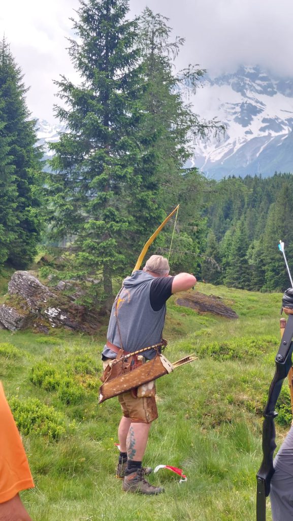 Bogenschütze spannt Jagdbogen auf grünem 3D-Parcours im Raurisertal, Natur im Hintergrund